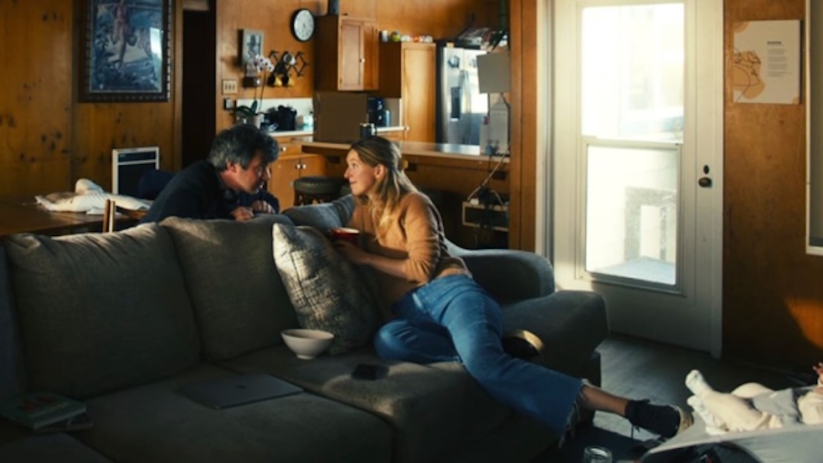 Director Nathan Fielder (left) and former Theranos CEO Elizabeth Holmes (center) captured in a candid, high-contrast shot inside a kitchen from the film 'You Can See Everything'.